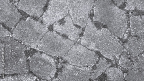 Monochrome close-up texture of old stone paving, featuring irregular rocks, rough surfaces, cracks, weathering, and small natural debris.