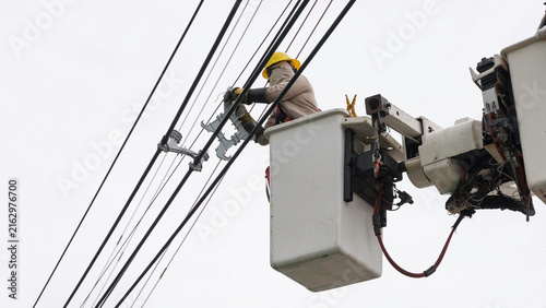 Electrician installing cable spacer on power lines from aerial bucket truck