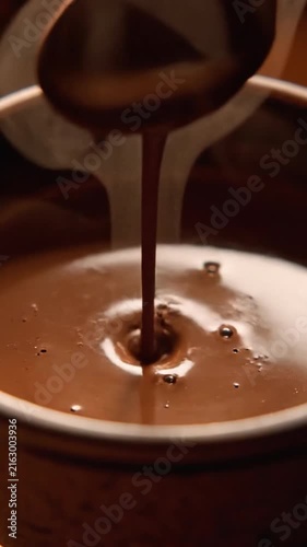 Stirring creamy hot chocolate with a spoon in a ceramic mug with steam and ripples