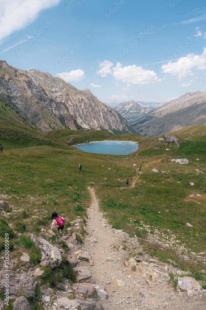 Fototapeta premium Randonneurs sur sentier de montagne face à un lac alpin, Queyras