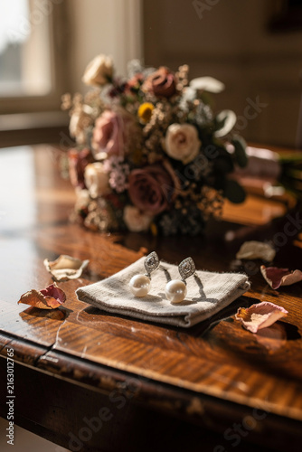 Elegant pearl earrings with bridal bouquet on wooden table