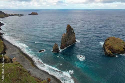 Aerial view of the dramatic sea stacks at Ribeira da Janela rising from the Atlantic Ocean with crashing waves on the dark volcanic pebble beach in Ribeira da Janela, Madeira, Portugal.