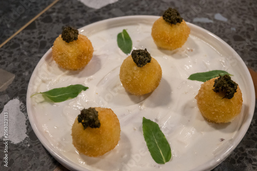 Golden arancini balls topped w dark caviar, served on a creamy white sauce with green garnish. Fusion cuisine, blending Italian technique with Georgian flair. 