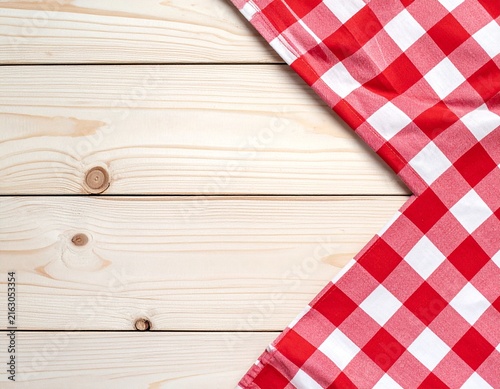 Red and white checkered tablecloth corner on light pine wood planks background, rustic picnic texture with copy space for food or text overlay design.

