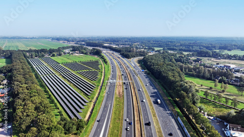 Aerial view of the A1 highway running through the landscape with an adjacent solar farm, green fields, and surrounding forests in Baarn, Utrecht, Netherlands.