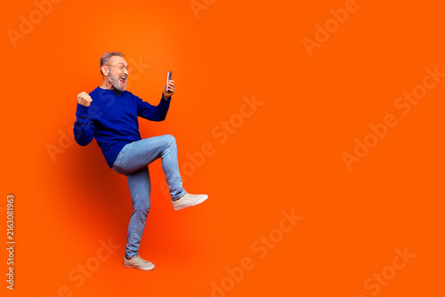 Konstfotografi Happy senior man cheering with smartphone in hand celebrating a win against a vi