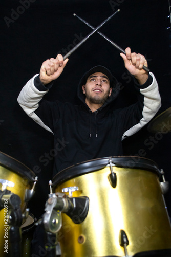 Fotografie Young male drummer in a black and white hoodie performing on a gold drum set against a black background