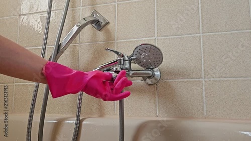 A hand in a bright pink rubber glove works on the chrome shower mixer to eliminate limescale; the image highlights the interaction with the plumbing fixture during the descaling process in a beige-til