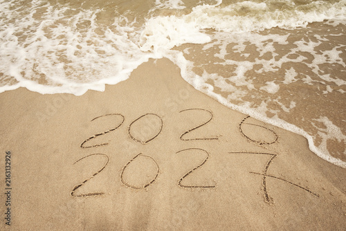 Inscription 2026 and 2027 numbers written on sand.  New Year 2026 replace 2027. Concept on the sea beach