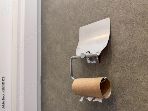 Canvas Print Close-up of empty toilet paper roll on modern metallic holder hanging on concrete style dark wall in domestic bathroom or restroom, concept of finished hygiene supplies, shortage of household product