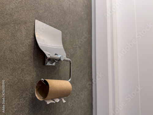 Photography Close-up of empty toilet paper roll on modern metallic holder hanging on concrete style dark wall in domestic bathroom or restroom, concept of finished hygiene supplies, shortage of household product