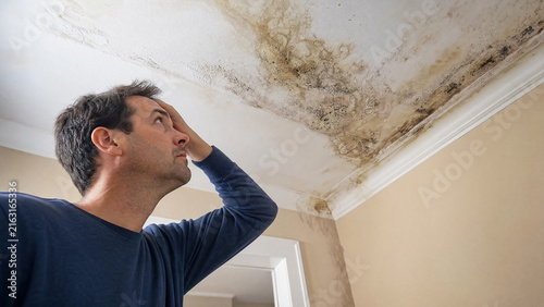 Worried man inspecting severe water stain and mold damage on house ceiling low angle view