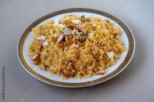 Fried crispy laccha semai dessert garnished with nuts raisins and grated coconut on ceramic plate. Traditional South Asian sweet dish prepared for Eid festival.