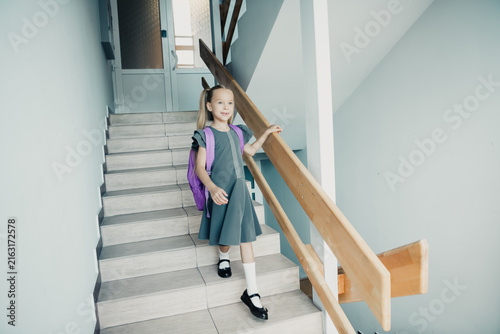 Foto Young schoolgirl with purple backpack walking down stairs in a bright school hal