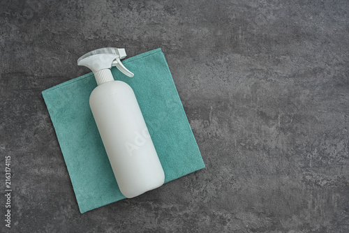 Blank white spray bottle and microfiber cleaning cloth on dark gray background, cleaning supplies flat lay with large copy space.