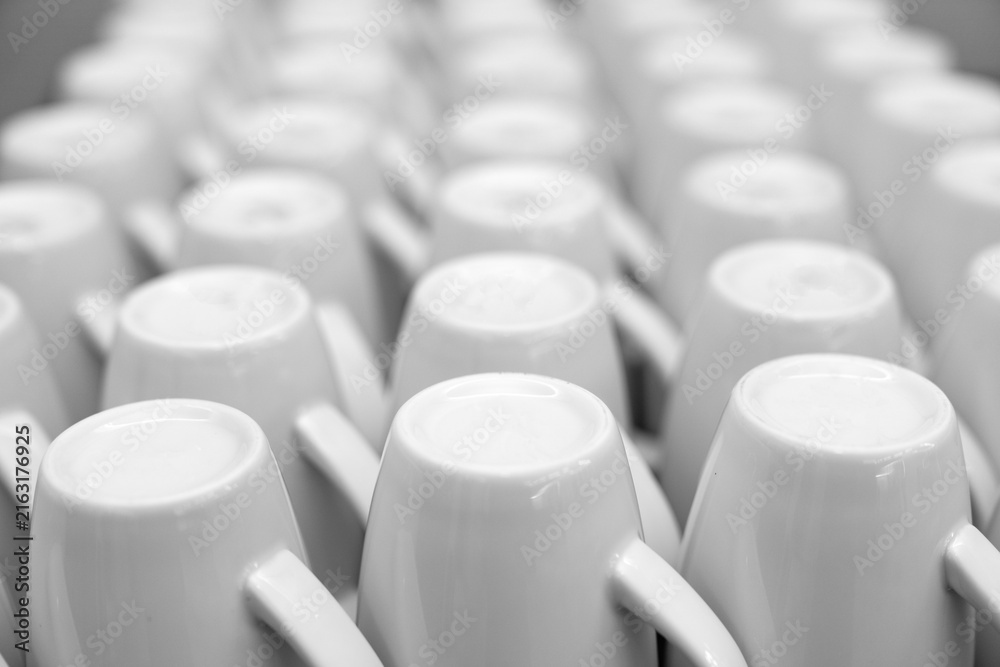 Fototapeta premium Clean row of empty white ceramic coffee mugs standing on table in minimalist cafe and restaurant kitchen, conceptual modern dishware texture pattern background for catering and office breakfast concep