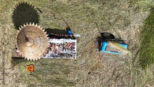 Aerial view of a traditional straw umbrella shading a display of handmade handicrafts on the floating reed islands of Lake Titicaca in Uros, Peru.