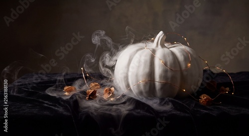 White pumpkin with foggy smoke and fairy lights on dark velvet table for Halloween decor