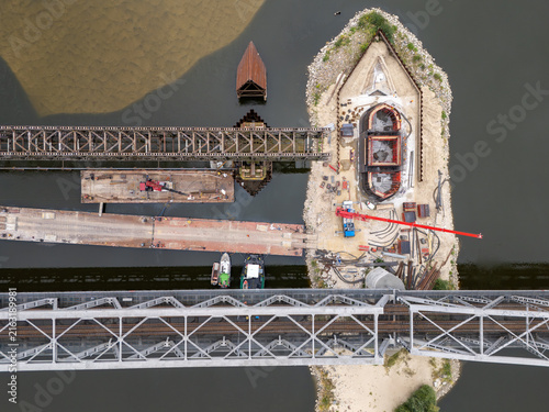 Aerial view of the bridge construction site on the Vistula River featuring steel trusses, heavy machinery, and a crane on a sandbank in Tczew, Poland.
