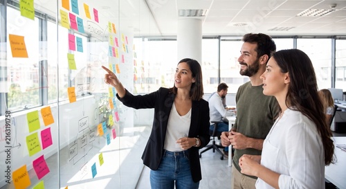 Business team planning agile project with sticky notes on glass wall in modern office