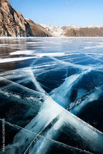 Blue transparent cracked ice and rocks on Baikal lake, Siberia, Russia.