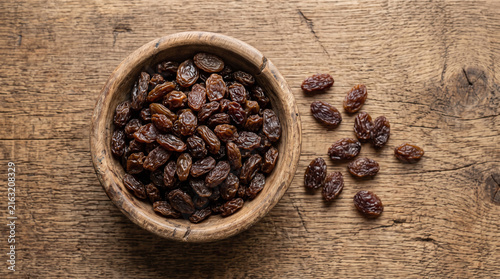Bowl of dark dried raisins on a rustic wooden table from a top view perspective