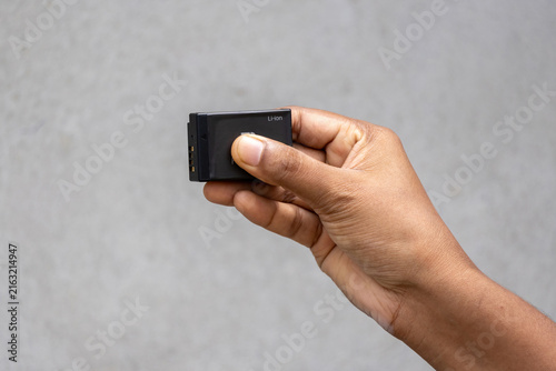 Human hand holding small rechargeable lithium ion battery pack for digital camera equipment. Essential accessory for electronic gadgets and power supply.