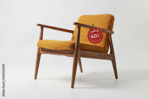 Mid-century modern armchair with yellow bouclé upholstery. Wooden lounge chair with red 40% sale tag. Retro furniture for interior design.