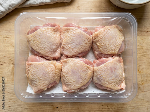Raw chicken thighs in a plastic food container on a rustic wooden table