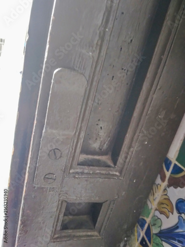 Fotografie Weathered wooden door frame featuring a vintage metal latch mechanism with exposed screws and peeling brown paint captured from a low angle in natural daylight