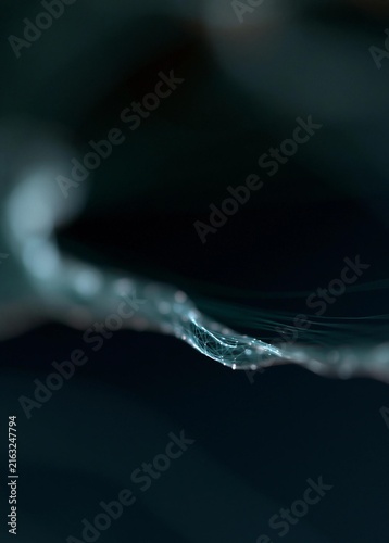 Close-up of a single drop of water on a dark background. the drop is in the center of the image, with a thin, white line extending from the bottom right corner to the top left corner.