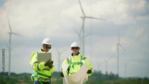 Engineers wearing safety helmets and jackets inspecting a wind turbine at wind farm at sunset. Concept renewable energy, sustainable technology wind power maintenance and environmental engineering.