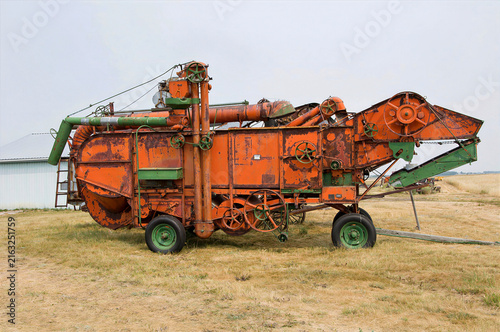 Konstfotografi A side view of a vintage mechanical threshing separator with rusty orange paint and green wheels