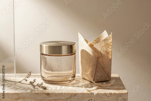 Glass jar with golden cap beside folded paper packaging on marble surface