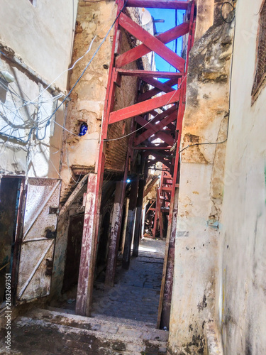 Fotografía Rusty red metal scaffolding bracing crumbling ancient stone walls in a narrow di