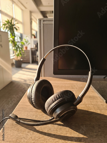 Customer Support Headset Resting Beside Blank Monitor on Wooden Office Desk