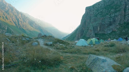 A first-person panoramic view from the feet of a hiker in dark pants and hiking boots, looking out over the mountain landscape ahead. Natural daylight, the atmosphere of an outdoor adventure