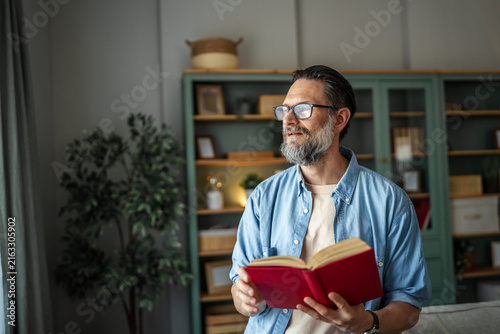 Konstfotografi Mature man reading book standing in home living room
