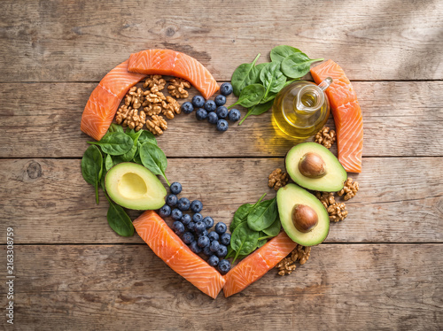 Heart-shaped arrangement of healthy foods with salmon, walnuts, and berries on wood table