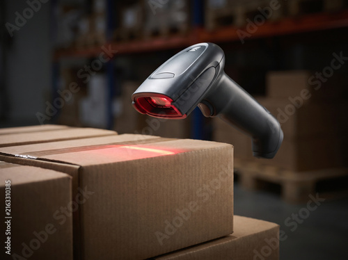 Handheld Barcode Scanner Beaming Light Over Cardboard Boxes in Warehouse