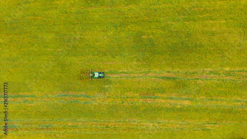 Aerial view of a green tractor working in a vibrant yellow-green field, creating patterns in the grass in Valldal, More og Romsdal, Norway.