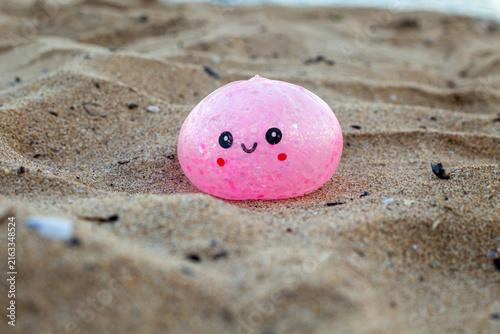 Cuadro en lienzo Pink kawaii dumpling toy with a cute smiling face lying on sandy beach, colorful