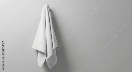 A clean white cotton towel hanging neatly on a modern wall hook against a soft neutral gray background for minimalist home bathroom interior design