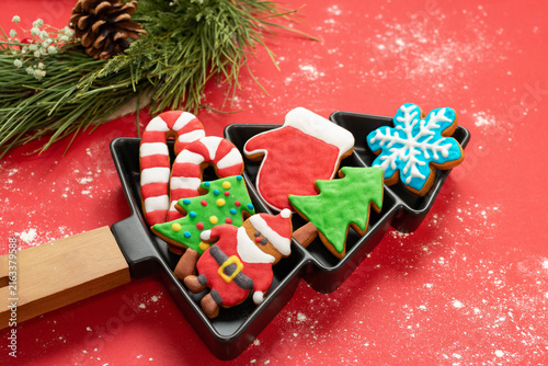 Festive Christmas gingerbread cookies served on a black tree-shaped plate, isolated on a red background and surrounded by pine branches. A festive holiday atmosphere for Christmas and New Year concept