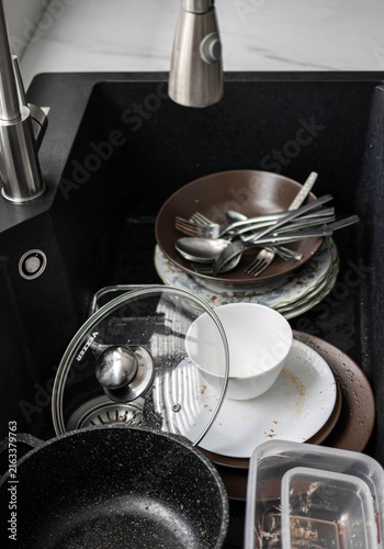 Dirty dishes, plates, and cutlery in a black kitchen sink. Messy pile of kitchenware after meal. Domestic chores and home cleaning concept