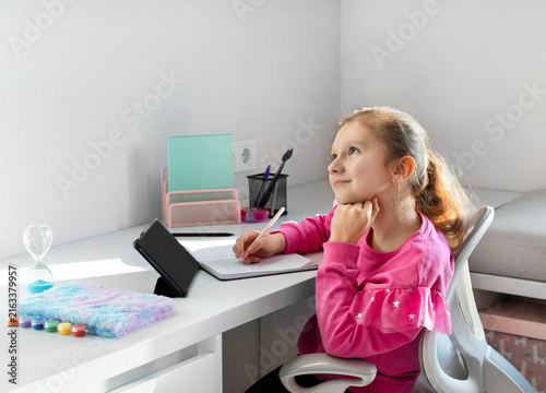 A dreaming girl leans her head on her hand at her desk during an online class on a tablet. Concept of school, homework and the beginning of the school year