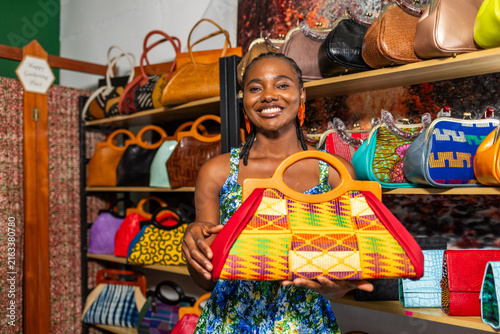 Картината върху платно African woman entrepreneur smiles, holding a colorful handcrafted handbag in her