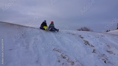 Slow motion two beautiful teenager girls ride from a snow-covered slide on round inflatable wheels.