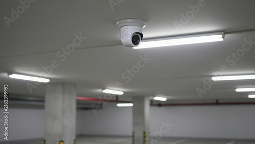 Ceiling-mounted dome surveillance camera monitoring a brightly lit modern underground parking garage