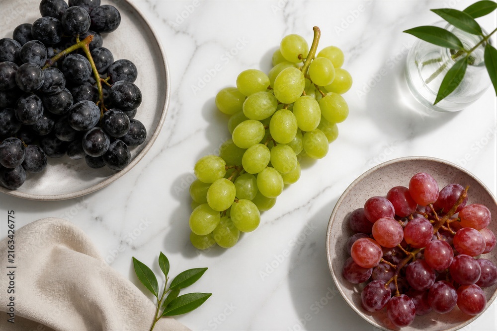 Fototapeta premium Mixed grapes arranged on marble countertop with plates